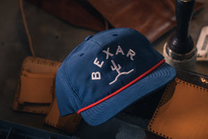 Blue Bexar Cap front view on a wooden table, showcasing the Bexar Goods logo patch